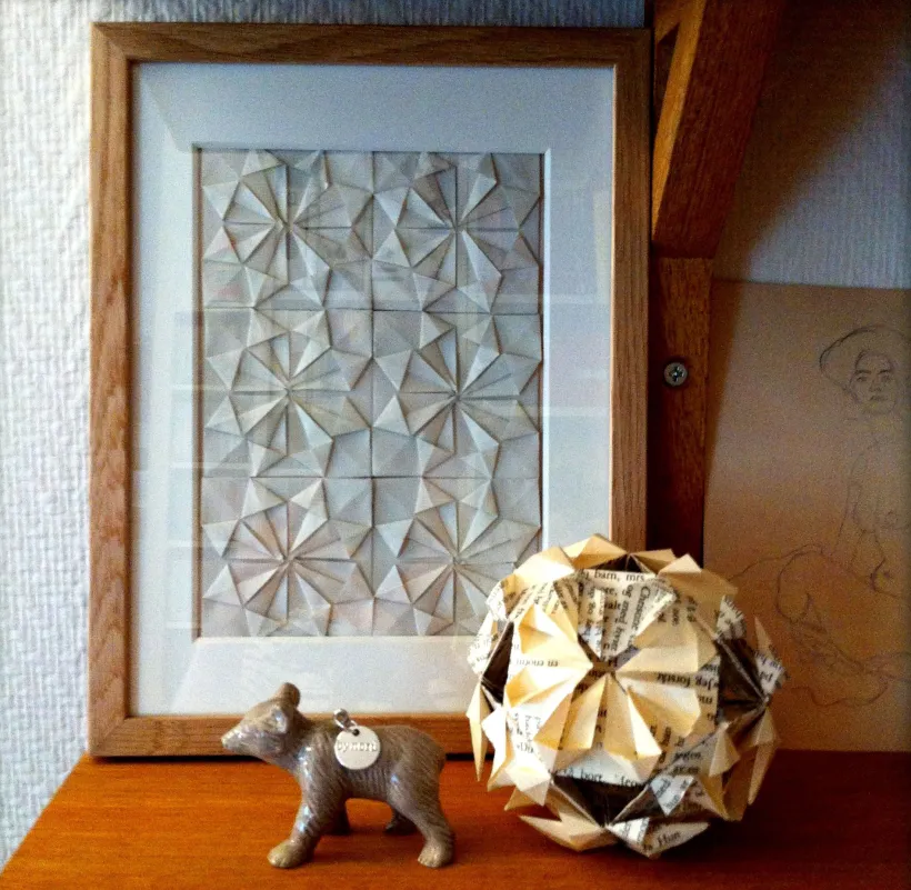 Stilleben med innrammet geometrisk papirkunst, en liten dyrefigur og en foldet papirkule laget av boksider