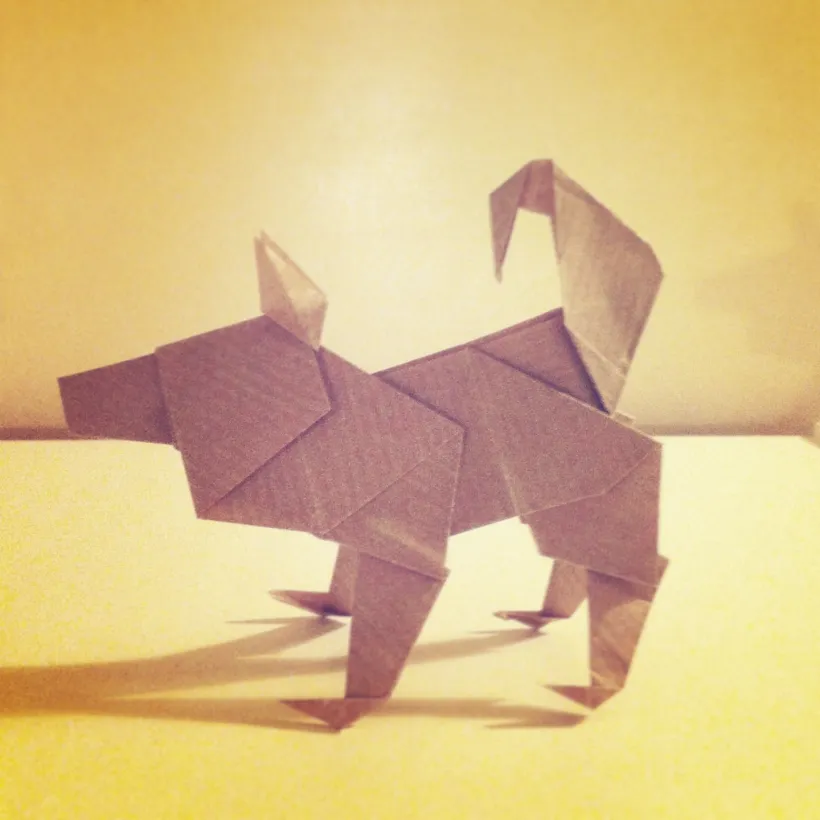 En brun origamipapirhund som står på et bord i varm, sepiatonet belysning.