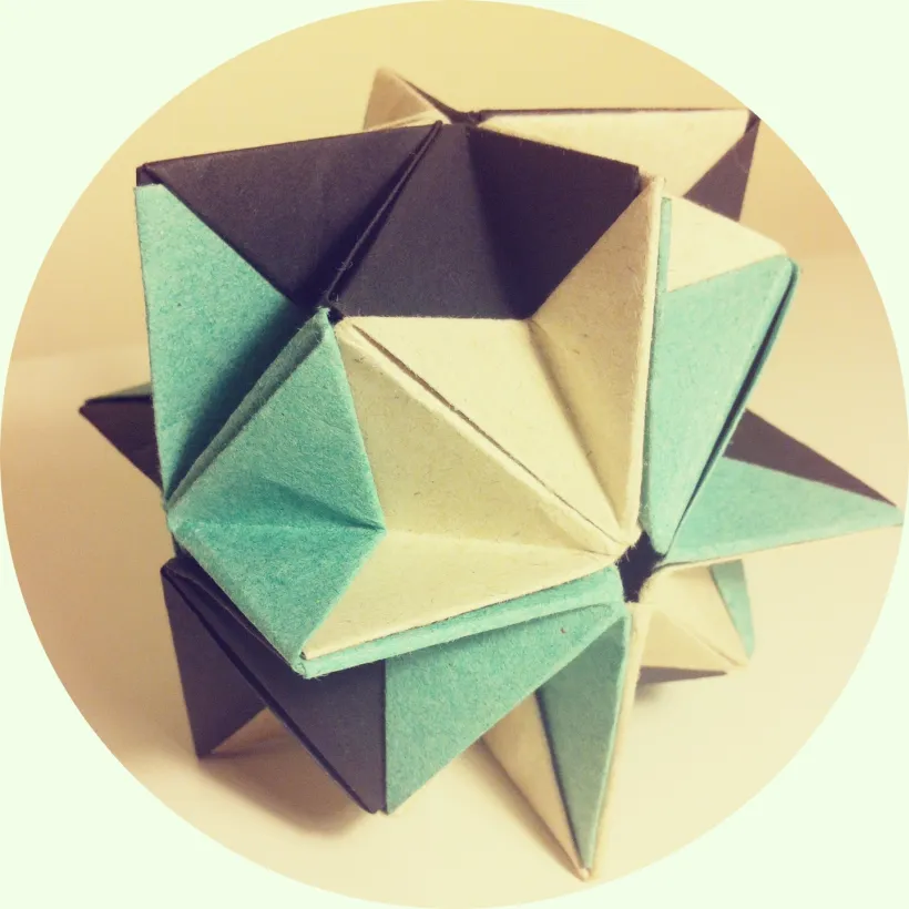Geometrisk origamistjerne i turkis, krem og mørke toner, fotografert i en rund ramme