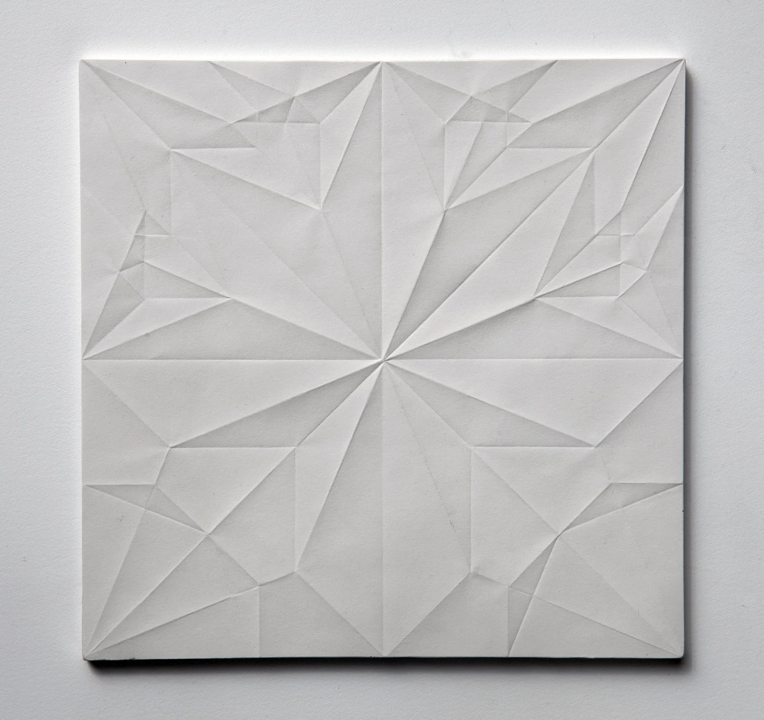 Hvitt teksturert panel med skarpe geometriske folder som former et stjernelignende mønster, minimalistisk stemning